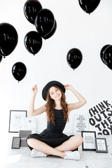 Cheerul beautiful young woman sitting and holding black balloons