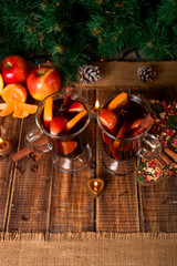 Christmas mulled wine with fruits, candles  and spices on wooden table. Xmas decorations in background. Two glasses. Winter warming drink  recipe ingredients around. Top view.