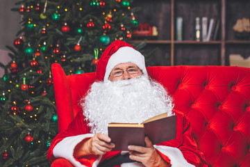 Santa Claus reading a letter sitting on a red sofa in the background Christmas tree. Christmas