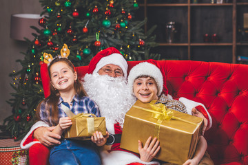 Fototapeta na wymiar Christmas, children and gifts. Santa Claus brought gifts to children. Joyful kids with gifts hugging Santa Claus