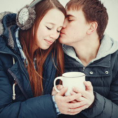 Loving couple in warm clothes drinking hot drink outdoors