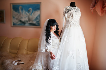 Young cute brunette bride looking at her wedding dress on manneq