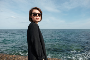 Woman in sunglasses and black coat on the seaside