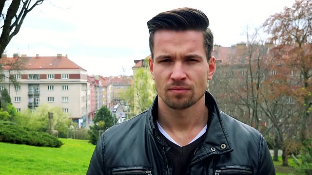 Young handsome serious man stands and shakes his head in park