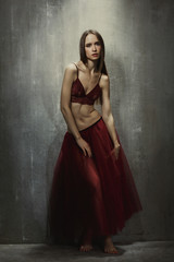 Fototapeta na wymiar Portrait of slim young girl dancer in red long skirt that sits o