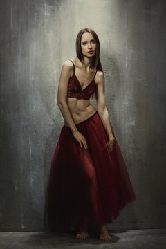 Portrait of slim young girl dancer in red long skirt that sits o