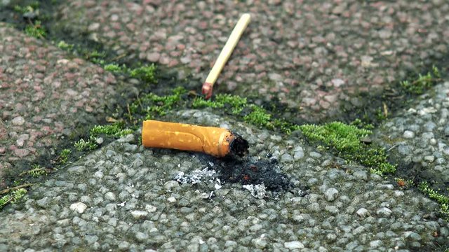 Man stubs out a cigarette on pavement - detail of cigarette