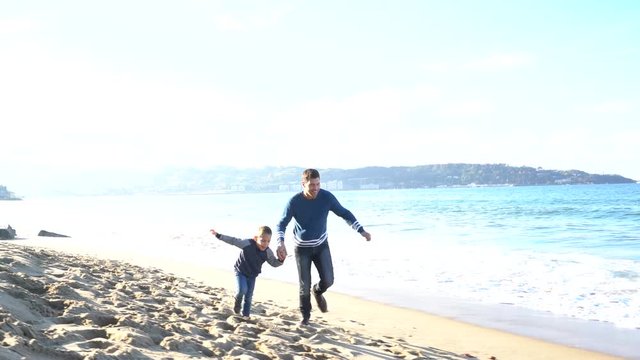 Father and son running on a sandy beach in autumn