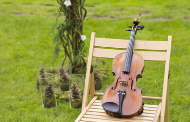 A beautiful violin on a chair outdoors. The concert on the open air. Festive concert. Wedding ceremony. Violin

