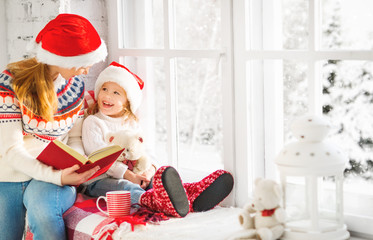 happy family mother and child daughter reading book on winter wi