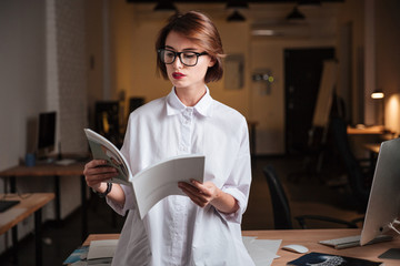 Serious young businesswoman reading magazine in office