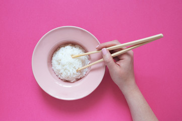 Pink plate with rice and chopsticks on the pink background