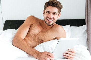 Cheerful man lying and using tablet in bed