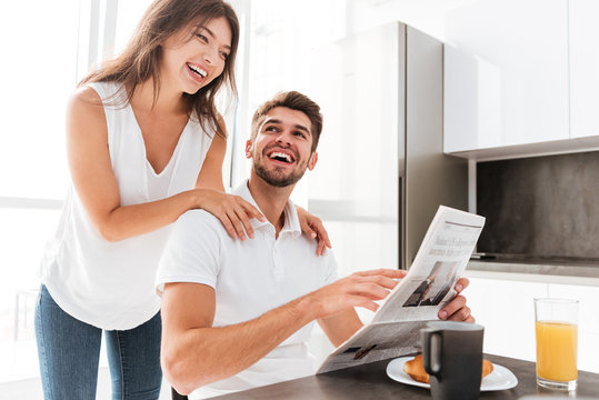 Couple with newspaper laughing and having breakfast on the kitchen