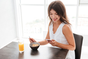 Woman having breakfast and using cell phone on the kitchen