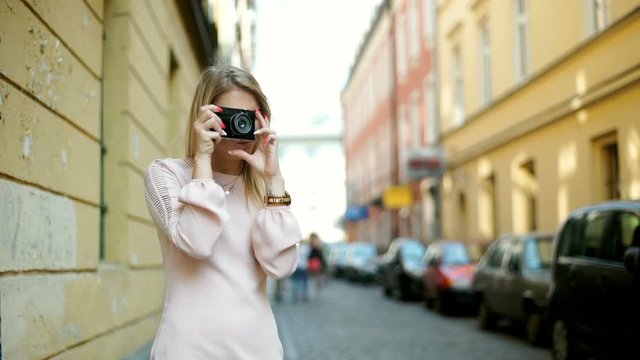 Elegant girl standing in alley and doing photos on old building by using camera
