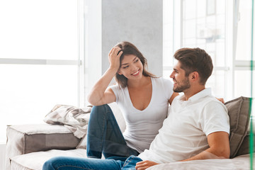 Cheerful beautiful young couple sitting and talking on sofa