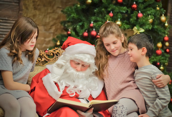 Fototapeta na wymiar Happy Santa reading book for childrennear Christmas tree