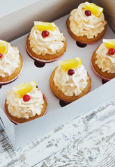 Vanilla cupcakes with a cap of cream on white wooden tablein the box