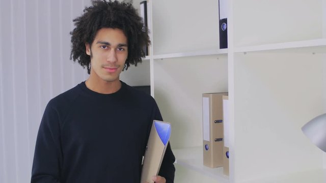 The young Afro-American costs near a case and holds in hand the folder