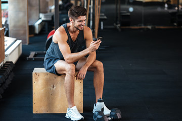 Fitness man sits on the box with phone