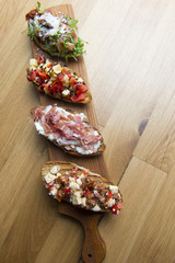 Bruschetta snacks with tomato, cheese, bacon, ruccola, parmesan, meat. Variety of small sandwiches on wooden background