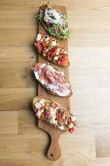 Bruschetta snacks with tomato, cheese, bacon, ruccola, parmesan, meat. Variety of small sandwiches on wooden background