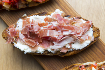 Bruschetta snacks with tomato, cheese, bacon, ruccola, parmesan, meat. Variety of small sandwiches on wooden background