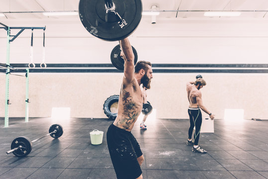 Young male cross trainer snatch lifting barbell in gym