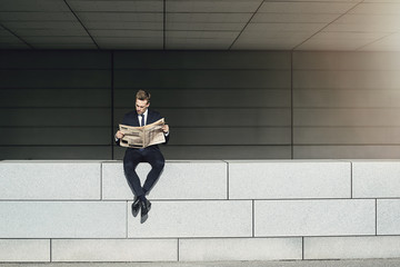 Fototapeta na wymiar Businessman sitting on brickwall and reading newspaper