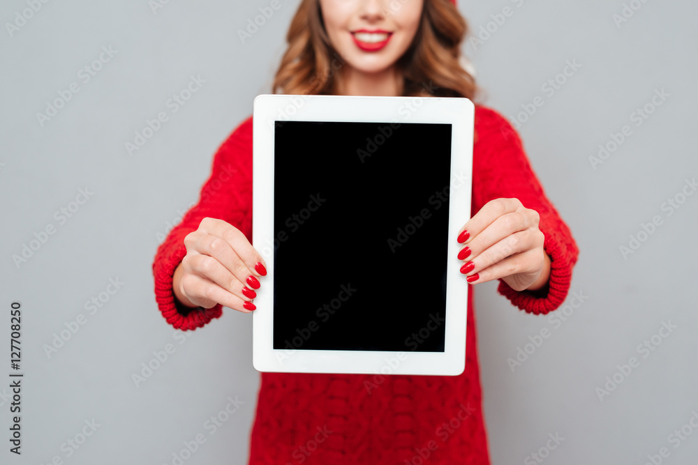 Poster Smiling woman in santa claus hat showing blank screen tablet