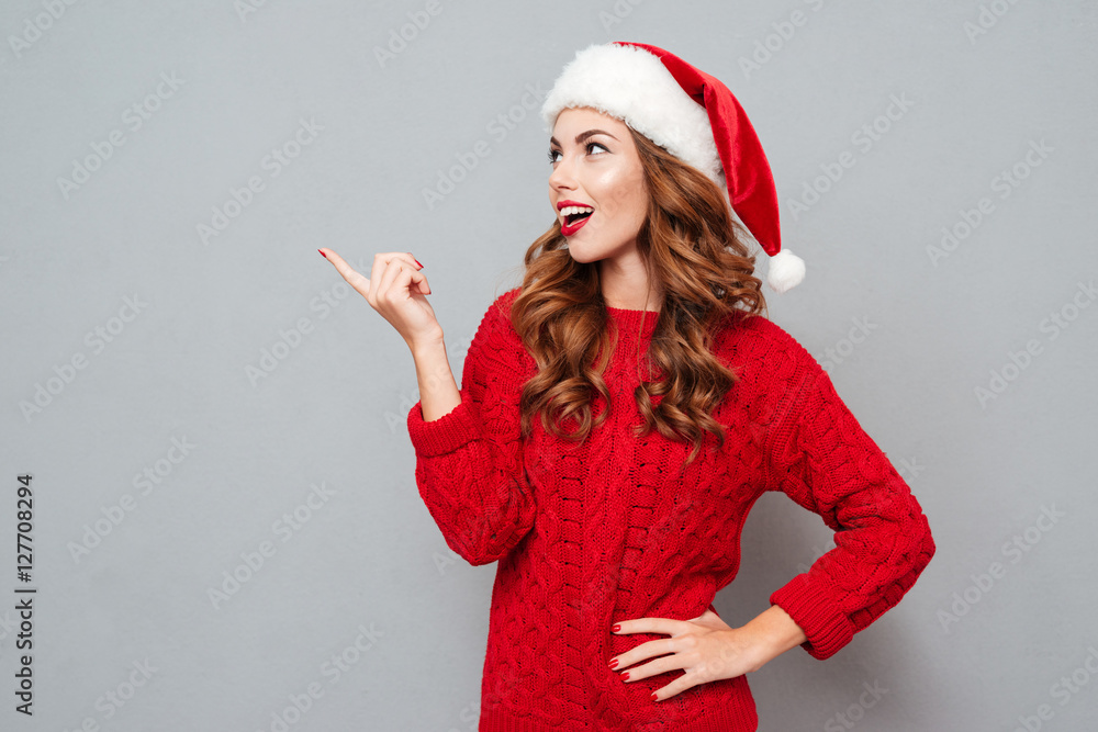 Sticker cheerful woman in santa claus hat standing and pointing away