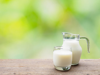 Milk jug and glass on wooden table of natural background
