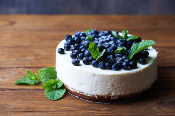 Sweet creamy blueberry cheesecake with fresh blueberries and mint leaves on a wooden background with copy space.