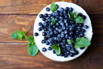 Sweet creamy blueberry cheesecake with fresh blueberries and mint leaves on a wooden background with copy space. top view.