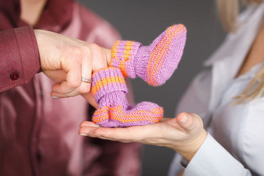 Cute orange knitted baby booties on hands. Pregnancy concept