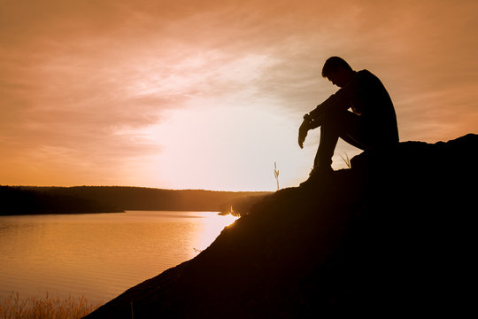 Silhouette of young man sitting on sunset or sunrise,