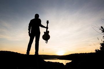 silhouette of musician with guitar at sunset or sunrise
