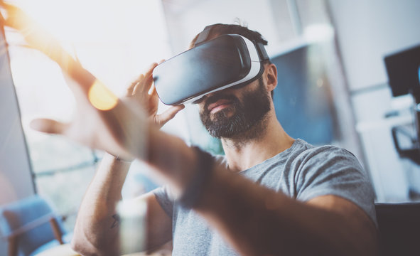 Closeup of bearded young man wearing virtual reality goggles in modern coworking studio. Smartphone using with VR headset. Horizontal, blurred.