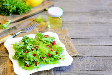 Fresh lettuce with pomegranate dressed with lemon juice and olive oil. Bright easy vegetarian food. Healthy salad on a plate, ingredients, fork, knife on wooden background with copy place for text