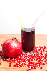 A glass of delicious pomegranate juice, pomegranate and pomegranate seeds on a table