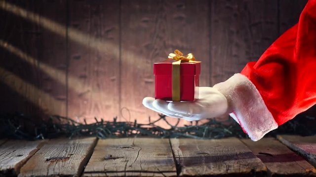 Santa Claus gives a gift box over wooden background with blinking Christmas tree garland. Full HD 1080p video footage