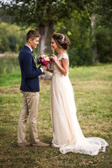 Bride and groom standing in the park, chatting and smiling. Summer time