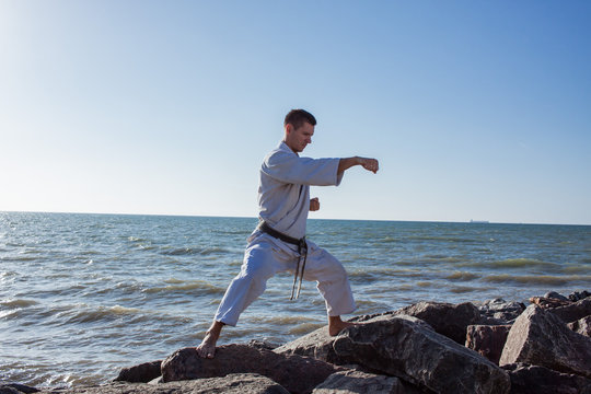 image of male karate fighter training on stones sea background