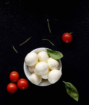 Top view of mozzarella cheese with cherry tomatoes and basil on a black slate surface