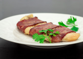 Grill white fish fillet baked in bacon with parsley on a white plate on black background front