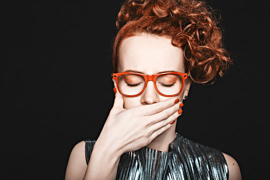 woman covered her mouth with his hand. beautiful red-haired woman with closed eyes in glasses holding her hand to her mouth. black background. closeup. the concept of coping with anxiety