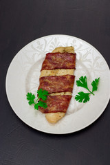 white fish fillet grill in bacon with parsley on a white plate isolated on black background