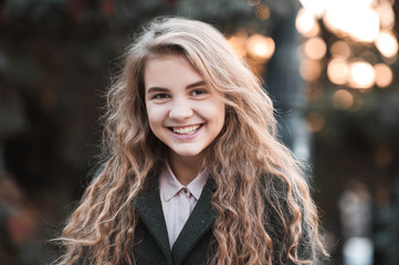 Obraz premium Smiling blonde teen girl 14-16 year old with curly hair wearing winter jacket over sunset at background. Looking at camera.