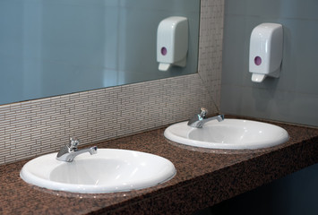 Empty public toilet room with sinks and taps.